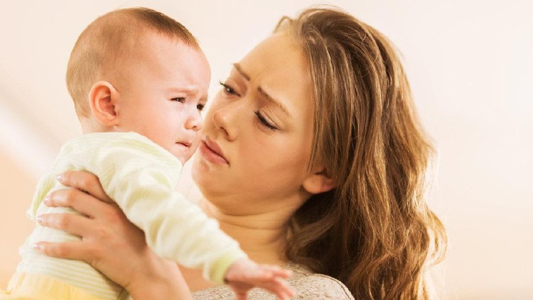 Young mother holding her baby boy who is crying.