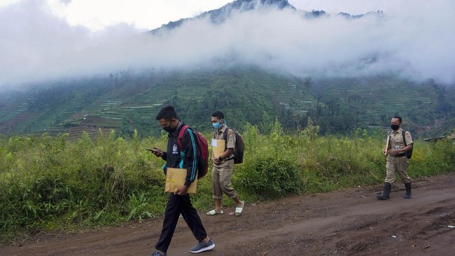 Kepala Sekolah SMP N 4 Bawang Mulud Sugito (kanan) dan guru Wiyata Bhakti berjalan kaki guna mengantar lembar tugas siswa langsung ke  rumahnya di Pranten, Kecamatan Bawang, Kabupaten Batang, Jawa Tengah.
