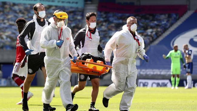 A medical team wearing protective suits enters the pitch to assist Arsenal's goalkeeper Bernd Leno after he got injured injured during the English Premier League soccer match between Brighton & Hove Albion and Arsenal at the AMEX Stadium in Brighton, England, Saturday, June 20, 2020. (Gareth Fuller/Pool via AP)