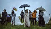 Perayaan Titik Balik Matahari People gather as some shield from the rain next to the closed Stonehenge, to celebrate the Summer Solstice, the longest day of the year, near Salisbury, England, Sunday June 21, 2020. (Ben Birchall/PA via AP)
