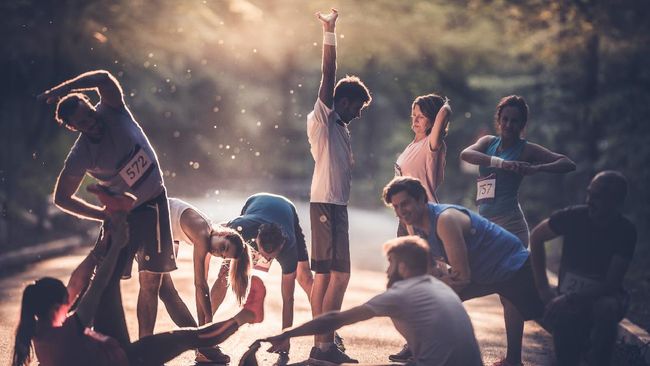 Marathon runners stretching and warming up before the race at sunset.