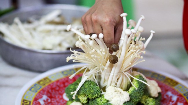 A closer look on human hand using enoki mushroom for garnishing as part of food preparation in Malaysia.