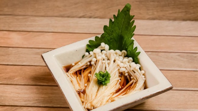 Japanese side dish called Enoki ponzu is boiled enoki mushroom with sweet and sour soy sauce called Ponzu topping with scallion and perilla leaf on brown wooden plate .