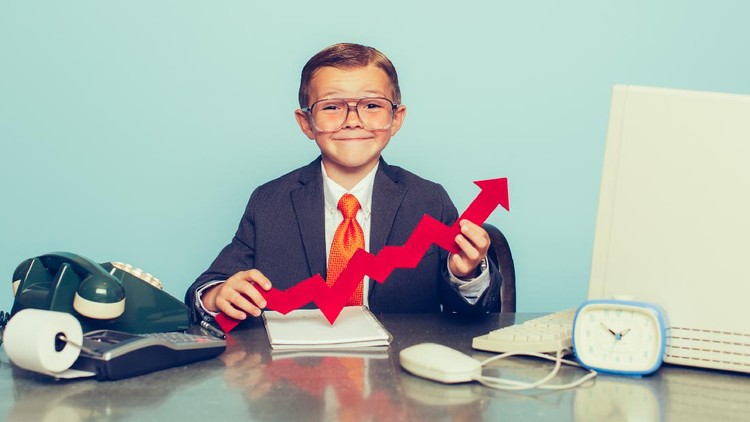 A young boy dressed as a businessman sits at his desk smiling as there is some good business happening. He sits at his desk with retro computer and phone.