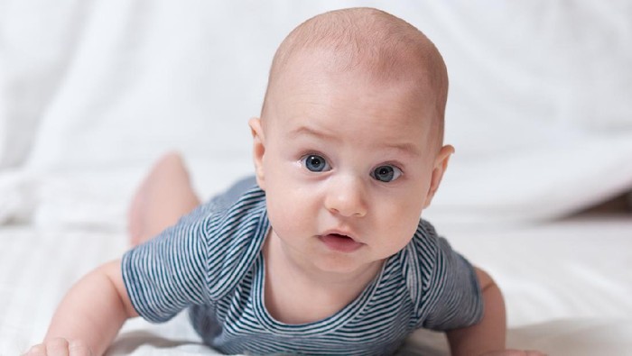 Happy cute four month old baby lying on his stomach on a bed in his room and smiling