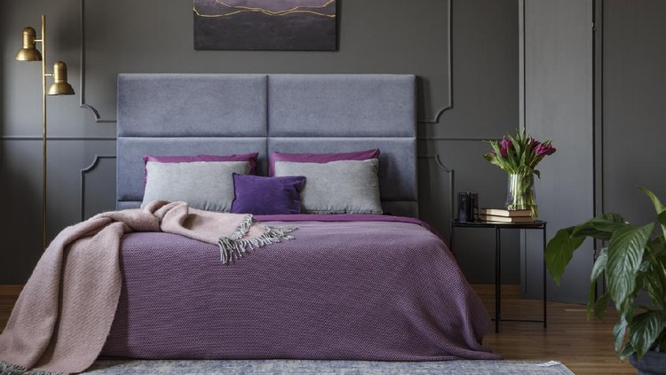Pastel blanket on pink bed in woman's bedroom interior with gold lamp and poster