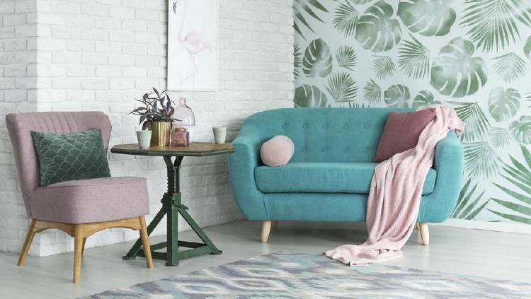 Green table with plant between pink chair and blue sofa in floral living room with wallpaper and poster