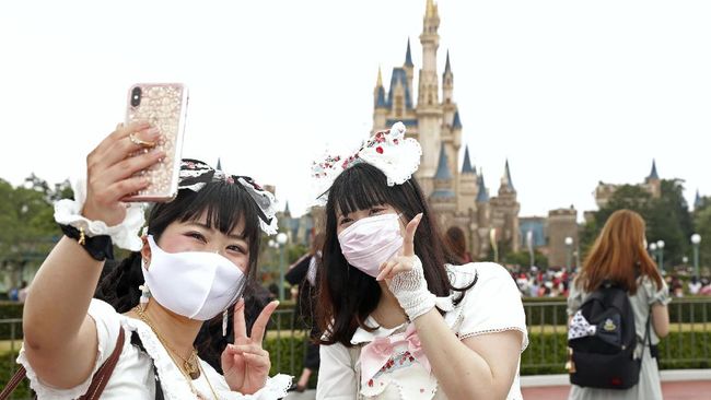 Visitors wearing face masks to protect against the spread of the new coronavirus take a selfie at Tokyo Disneyland in Urayasu, near Tokyo, Wednesday, July 1, 2020. Tokyo Disneyland reopens for the first time in four months after suspending operations due to coronavirus concerns. (Kyodo News via AP)