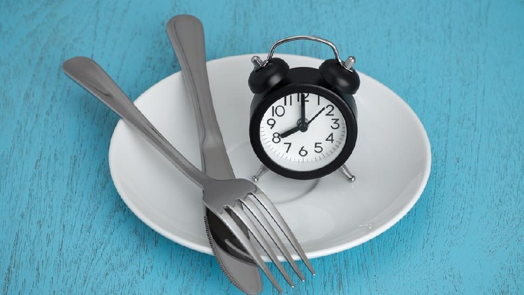 Intermittent fasting concept with clock on white plate, fork and knife on blue table