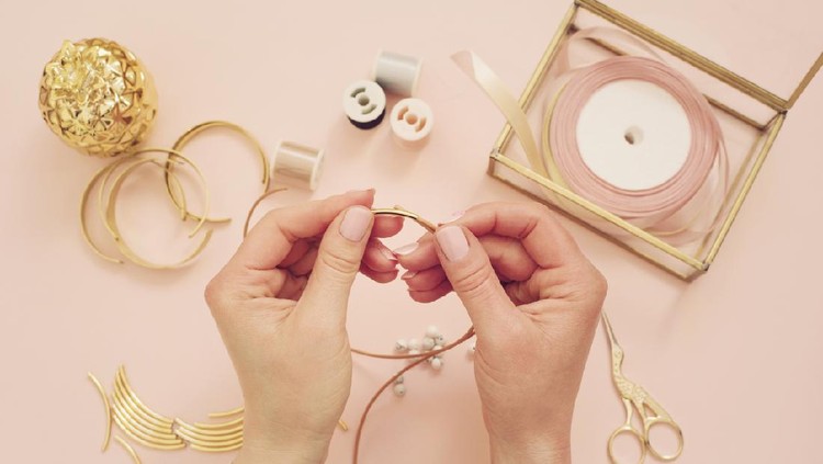 Jewelry designer workplace. Woman hands making handmade jewelry. Freelance fashion femininity workspace in flat lay style. Pastel pink and gold