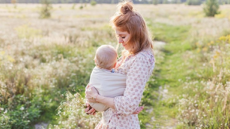 Little baby boy and his mother walking in the fields. Mother is holding and tickling her baby, babywearing in sling