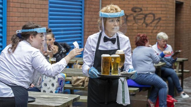 Staff wearing PPE (personal protective equipment) in the form of face shields and gloves serve people enjoying a drink in Belfast city centre on July 3, 2020, as pubs open their doors after the enforced closure due to the coronavirus pandemic. - Pubs, cafes, restaurants and hotels in Northern Ireland are permitted to reopen from Friday as relaxations of the coronavirus restrictions continue. (Photo by Paul Faith / AFP)