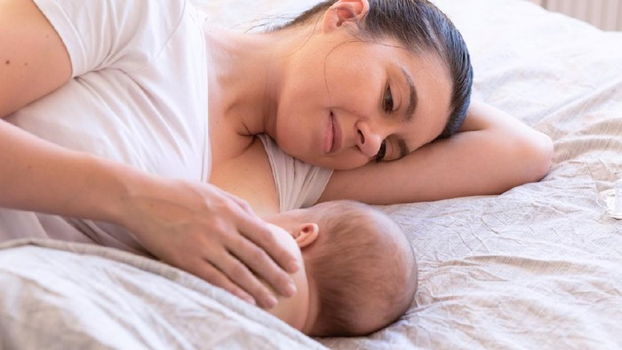 Smiling mother breastfeeding her baby daughter while being at home.