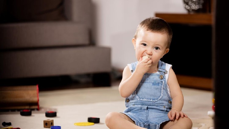 Happy baby eating banana in living room.