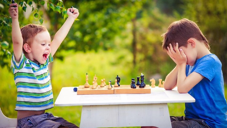 586945434 two young chess players outdoors. boy rejoices won a game of chess. sad opponent covered his face, and upset losing