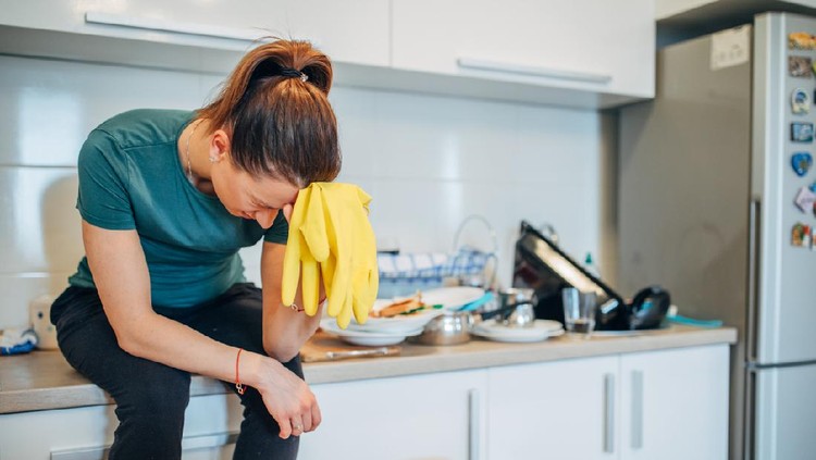tired modern 40 years old housewife in green apron and pink rubber gloves with spray bottle of cleaning supplies, brush and yellow wipe wet cleaning floor in the modern house in sunny day.