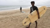 PANTAI KUTA BALI DIBUKA KEMBALI A man carries his surfboard at Kuta beach, Bali, Indonesia on Thursday, July 9, 2020. Indonesia's resort island of Bali reopened after a three-month virus lockdown Thursday, allowing local people and stranded foreign tourists to resume public activities before foreign arrivals resume in September. (AP Photo/Firdia Lisnawati)