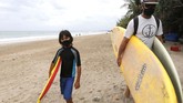 PANTAI KUTA BALI DIBUKA KEMBALI Tourists wearing face masks carry their surfboard at Kuta beach, Bali, Indonesia on Thursday, July 9, 2020. Indonesia's resort island of Bali reopened after a three-month virus lockdown Thursday, allowing local people and stranded foreign tourists to resume public activities before foreign arrivals resume in September.(AP Photo/Firdia Lisnawati)