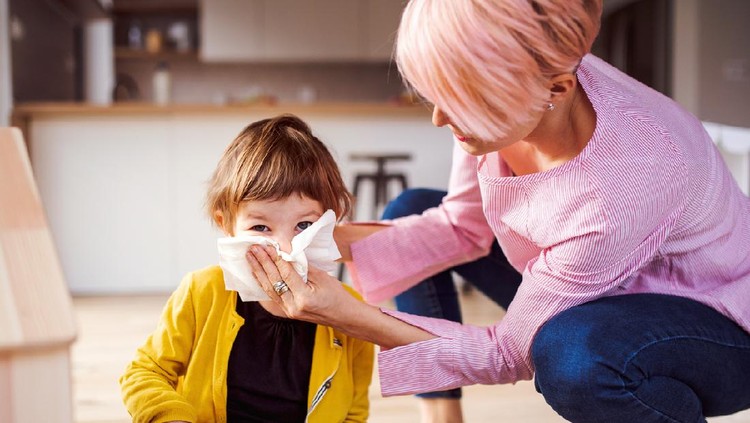 Young mother blowing her small daughter's nose when playing at home.