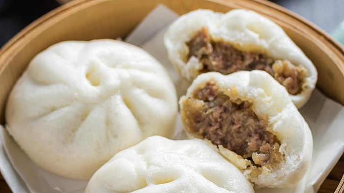 Delicious baozi, Chinese steamed meat bun is ready to eat on serving plate and steamer, close up, copy space product design concept.