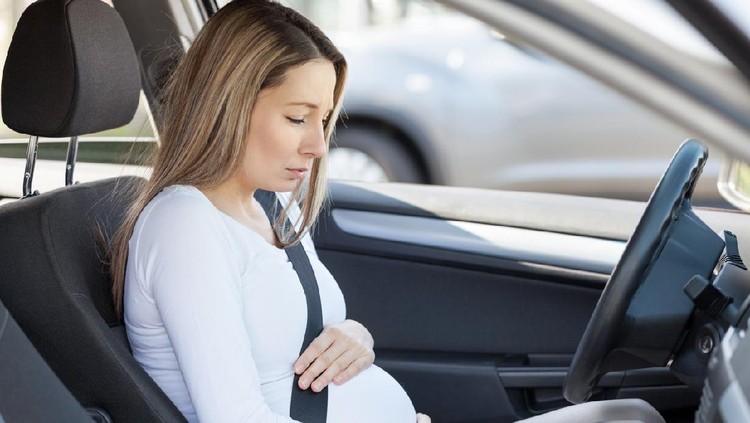 Young pregnant woman behind the steering wheel having contractions