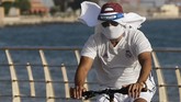 Kasus Virus Corona Meningkat di Arab Saudi A vacationer rides his bicycle while wearing a face shield and mask to help prevent the spread of the coronavirus, at the Red Sea beach in Jiddah, Saudi Arabia, Thursday, July 9, 2020. (AP Photo/Amr Nabil)