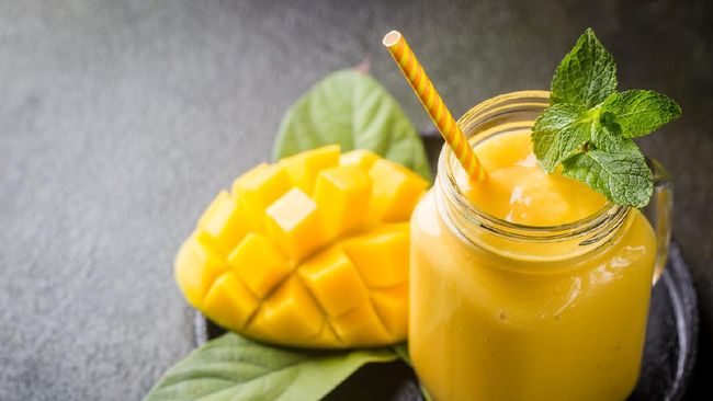 Refreshing and healthy mango smoothie in a glass with fresh fruit over stone background with copy space