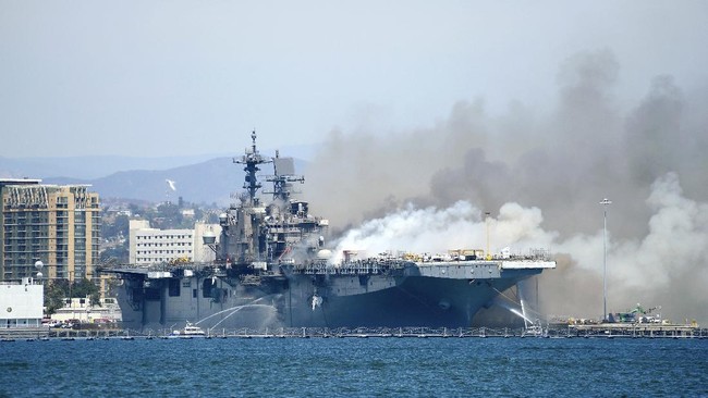 In a photo provided by the U.S. Navy, Port of San Diego Harbor Police boats fight a fire aboard the USS Bonhomme Richard at Naval Base San Diego, Sunday, July 12, 2020. Twenty-one people suffered minor injuries in an explosion and fire Sunday on board a ship, military officials said. The blaze was reported shortly before 9 a.m., said Mike Raney, a spokesman for Naval Surface Force, U.S. Pacific Fleet. Seventeen sailors and four civilians were hospitalized with “non-life threatening injuries,” Raney said in a brief statement. (Lt. John J. Mike/U.S. Navy via AP)