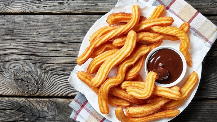 churros - Traditional Spanish and Mexican dessert on a white plate with chocolate sauce on an old grey rustic wooden table, horizontal view from above, close-up, flatlay
