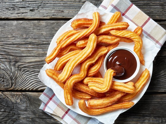churros - Traditional Spanish and Mexican dessert on a white plate with chocolate sauce on an old grey rustic wooden table, horizontal view from above, close-up, flatlay