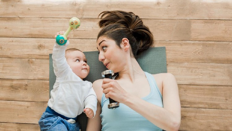 Top view of mother with baby boy lying on floor and playing with dumbbells