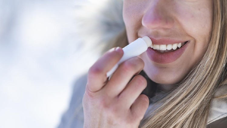 Portrait of young female applying lip balm in winter. Portrait of a beautiful woman in snow with application of the protective cream to the lips