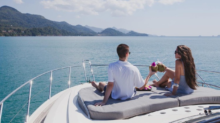 couple enjoying honeymoon onboard of luxury boat, luxurious yacht in tropical sea, man and woman drinking coconuts and relax