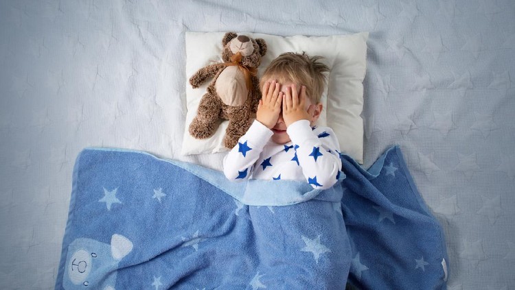 Three years old child crying in bed. Sad boy on pillow in bedroom