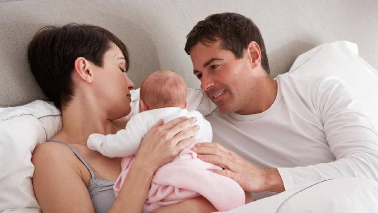 Parents Cuddling Newborn Baby In Bed At Home Lying Down Relaxing