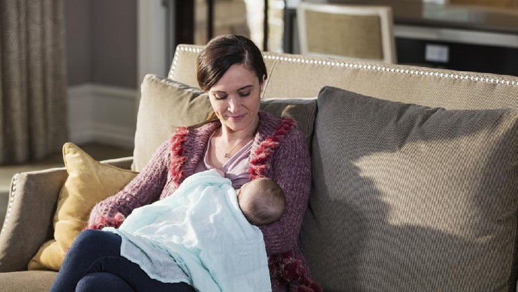 A mid adult woman in her 30s, holding her beautiful 2 month old baby girl, sitting on a sofa at home, nursing.