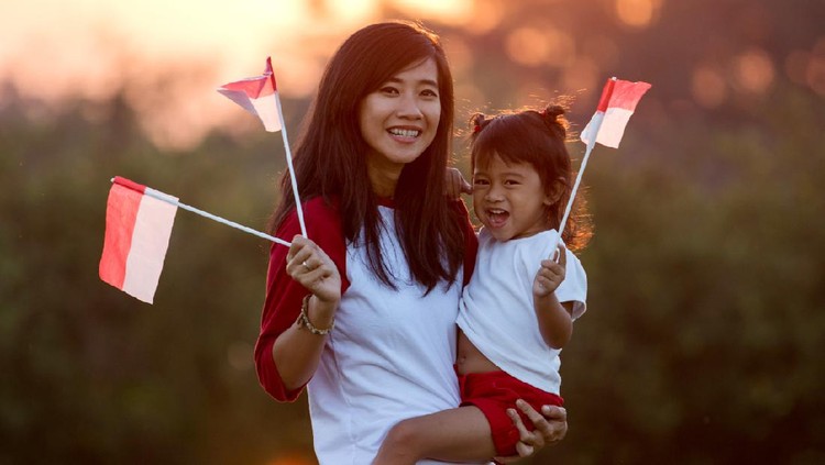Beautiful young mother with her daughter celebrating indonesia independence day by raising flag under the sunset sky