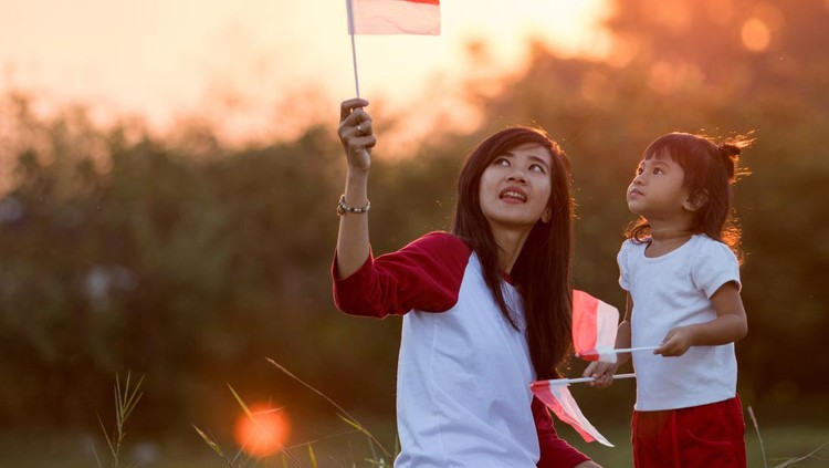 Beautiful young mother with her daughter celebrating indonesia independence day by raising flag under the sunset sky