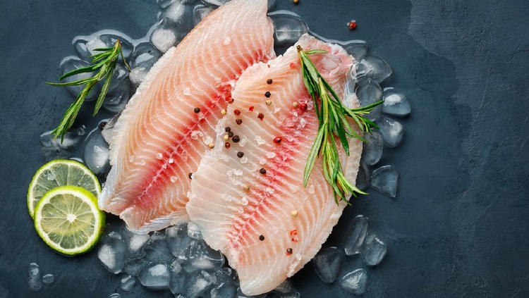 Fresh fish fillet of sea bass in ice on a dark slate background. Top view.