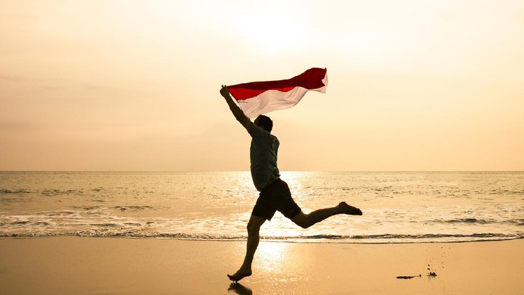 young man running on the  beach carrying Indonesia flag
