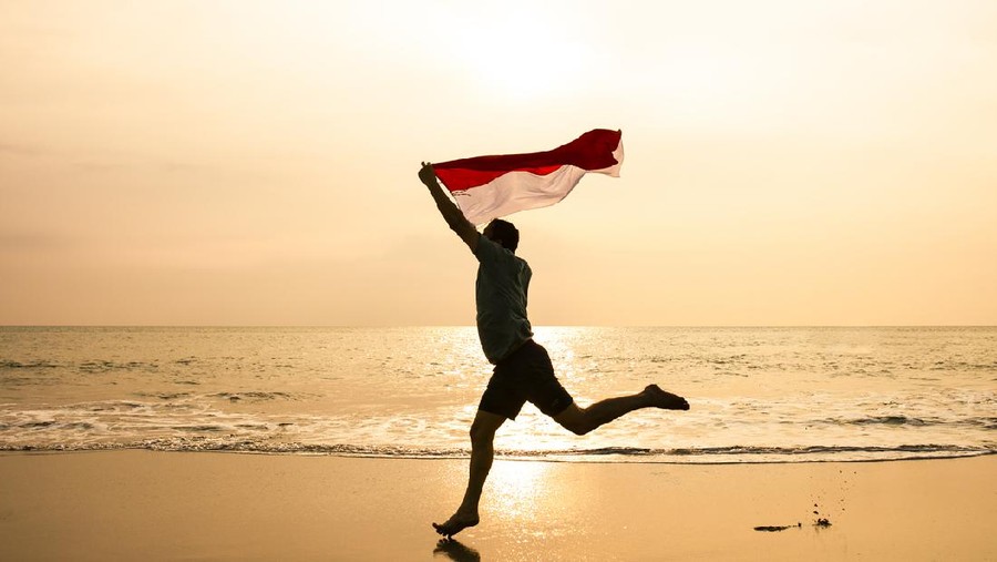 young man running on the  beach carrying Indonesia flag