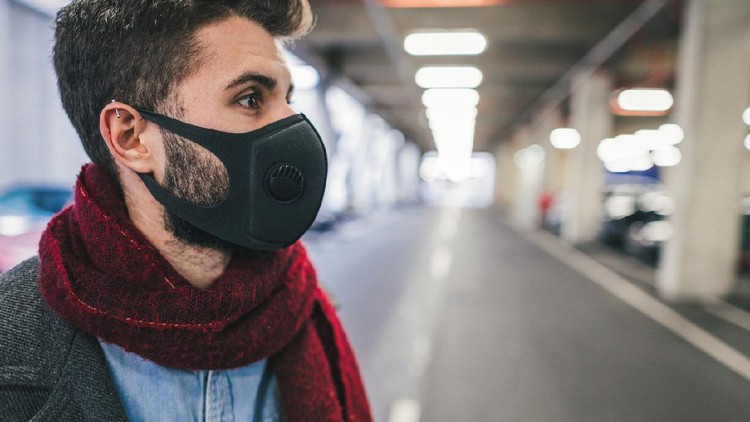 Side view image of young man wearing anti-smog mask for health and lungs protection in the city. City pollution concept