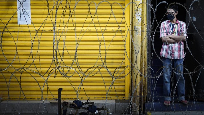 A man wearing a face mask stands behind barbed wire in s locked down area due to the new coronavirus in Kuala Lumpur, Malaysia, Friday, May 15, 2020. Despite a sharp drop in infections, Malaysia's leader said restrictions to fight the coronavirus will be extended by four more weeks until June 9. The government has already let most businesses reopen with strict conditions to help revive a hard-hit economy. But mass gatherings are still barred, with schools, cinemas and houses of worship staying shut, group sports prohibited and interstate travel banned. (AP Photo/Vincent Thian)