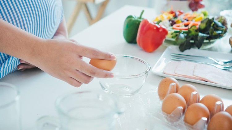 Woman cracking an egg into a bowl with  standing by in kitchen. Mother pregnant cooking in kitchen.