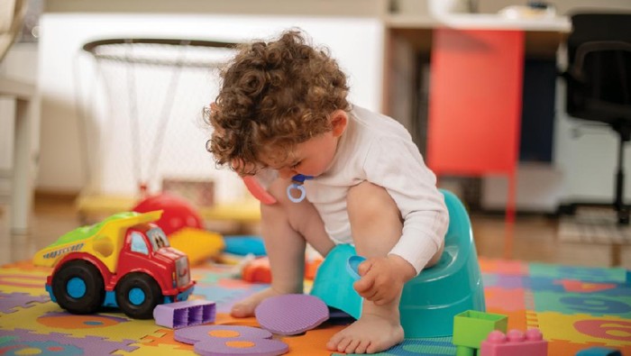 Toddler playing with a foam tiled flooring while sitting on a potty.