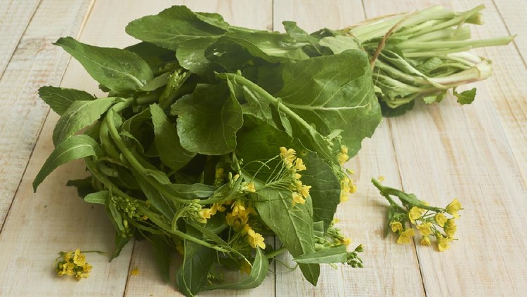 Edible mustard leaves and flowers (brassica juncea) on a wooden rustic table. The leaves and flowers of mustard are known as a very nutritious antioxidant food. Studio shot. High angle view. Close-up. Natural day lighting. Inddors photography. Horizontal composition. Copy space.