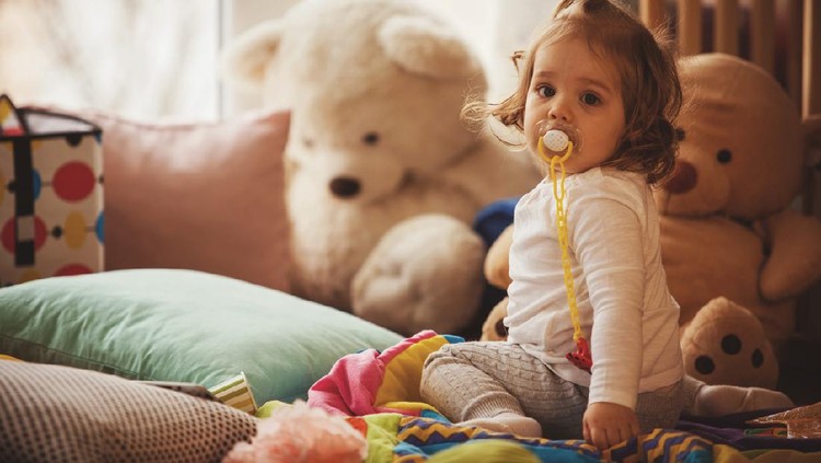 Ilustrasi empeng Copy space shot of little girl with pacifier sitting on the floor of living room. She is surrounded with stuffed toys and soft pillows.