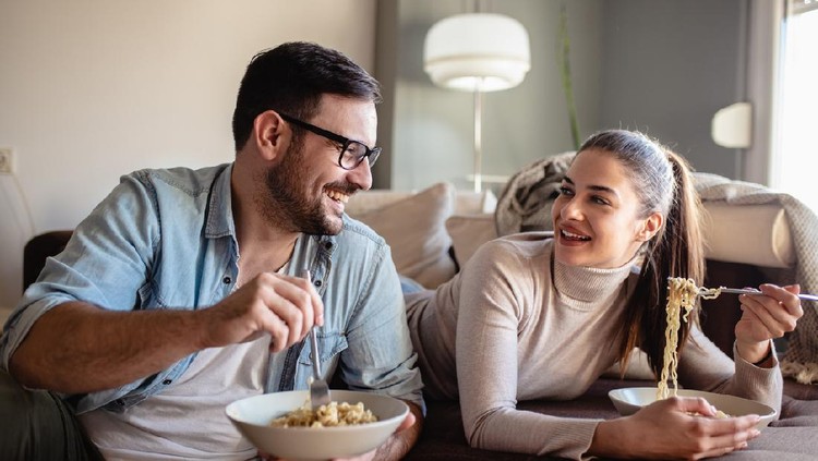 Young couple is in eating lunch at home together in the living room and they are looking at each other