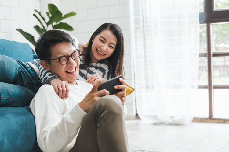 Lifestyle Asian couple man and woman playing game on mobile phone together at home, Asian couple family lifestyle concept