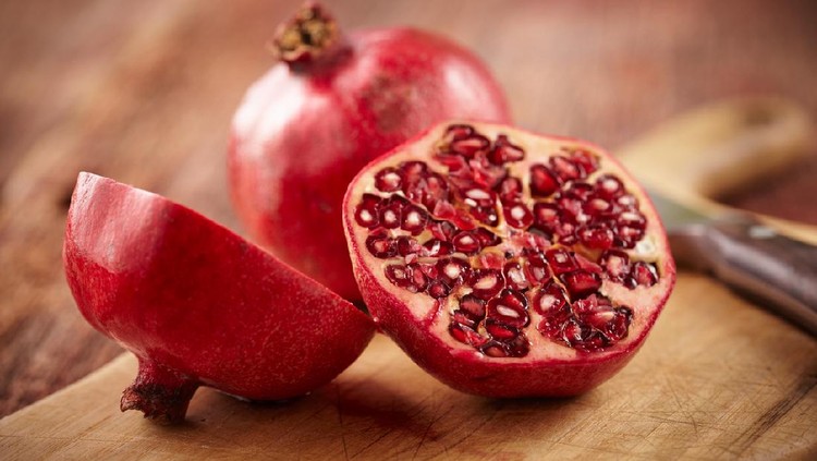 Buah delima Sliced pomegranate on cutting board with knife and whole pomegranate behind. Shot with shallow focus on sliced fruit.